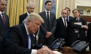 Donald Trump signing paper and white men surrounding him.