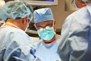 Close up of a surgeon in full blue scrubs and glasses.