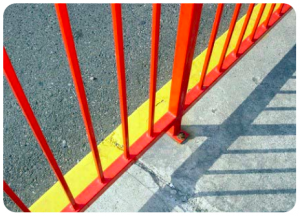 The edge of an orange fence casts a shadow on the sidewalk. The bright orange fence is aligned with a yellow strip on the ground.