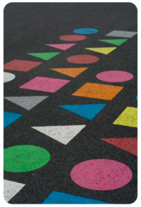A pattern of circles, squares, and triangles in bright colors contrasted on an asphalt surface.
