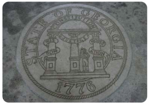 A picture of the Seal of the state of Georgia (dated 1776), engraved into stone. The description on the seal has three columns labeled “wisdom,” “justice,” and “moderation,” with a semi-circle labeled “constitution connecting the three.