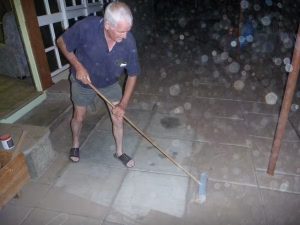 A white, older man sweeps away dust on tile outside a home in the dark in Western Australia.