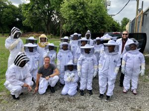 Brian Peterson-Roest kneels and smiles among a group of young students in full bee suits in a field
