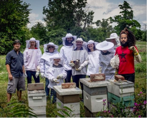 Antonio Rafael stands behind beehives with a group of nine in a field