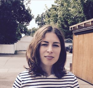 Bridget Mendel-Lee in black and white striped shirt stands outside