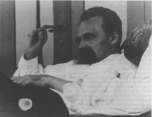 A black-and-white photograph of Nietzsche lounging on a sofa. His hand is in the air as if he is in the midst of saying something.