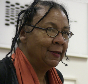 bell hooks face mid-speech. She is wearing glasses, an orange scarf and braids.