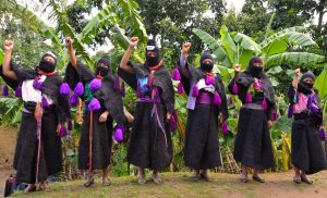6 women of the Zapatistas in full uniforms raise their right fists.