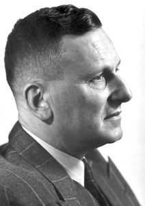 Side portrait of a Nobel Prize winner Paul Hermann Muller, a caucasian man with short hair wearing a striped suit.